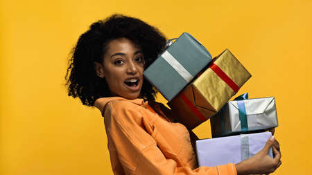 amazed african american woman with braces holding gift boxes isolated on yellowの写真素材
