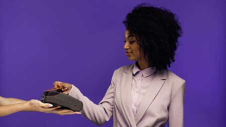 cheerful african american businesswoman paying with credit card isolated on purpleの写真素材