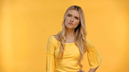 Angry blonde woman in blouse looking at camera isolated on yellowの写真素材