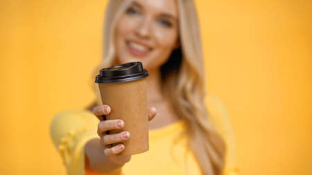 Coffee to go in hand of blurred woman isolated on yellow