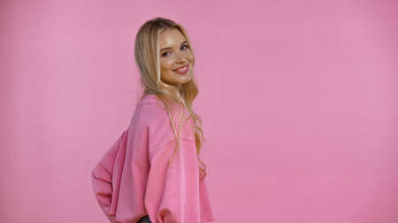 Pretty blonde woman smiling at camera isolated on pinkの写真素材