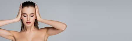 young woman with naked shoulders touching wet hair isolated on grey, bannerの写真素材
