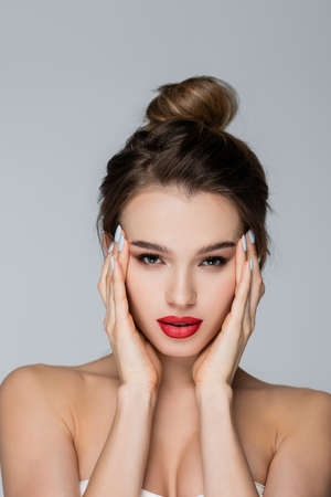 charming woman with perfect skin and red lips looking at camera isolated on grayの写真素材