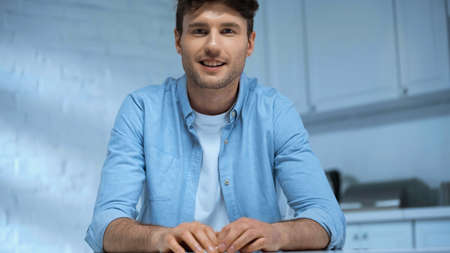 man in blue shirt smiling at camera while sitting in kitchen