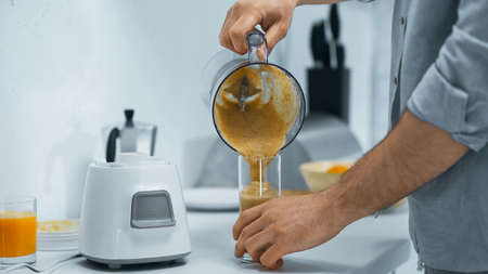 cropped view of man pouring fresh smoothie into glass in kitchen