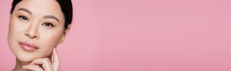 Asian woman with makeup looking at camera isolated on pink, bannerの写真素材