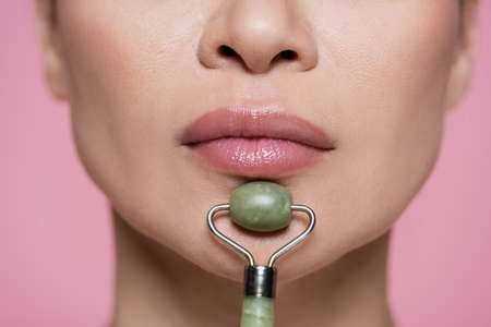 Cropped view of jade roller near chin of woman isolated on pinkの写真素材