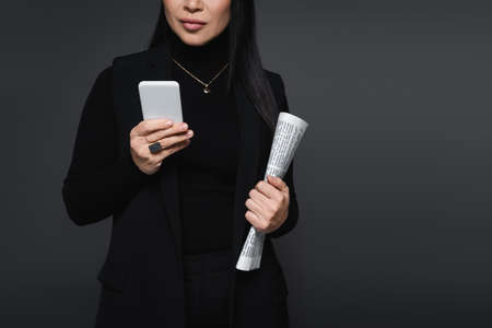 Cropped view of stylish woman holding newspaper and smartphone isolated on dark grayの写真素材