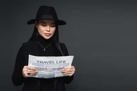 Stylish asian woman reading newspaper isolated on dark grayの写真素材