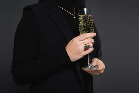 Cropped view of woman in jacket holding glass of champagne isolated on dark grayの写真素材
