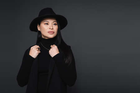 Fashionable asian woman in fedora hat looking away isolated on dark grayの写真素材