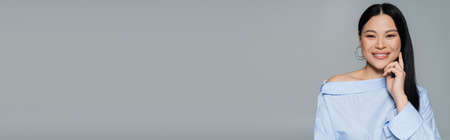 Positive asian woman in blue blouse looking at camera isolated on grey, bannerの写真素材