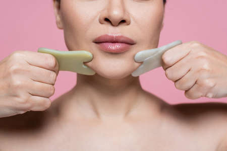 Cropped view of woman massaging chin with jade stones isolated on pinkの写真素材