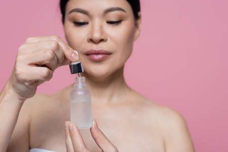 Bottle of serum in hands of blurred asian woman isolated on pinkの写真素材