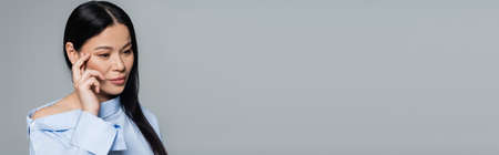 Thoughtful asian woman in blouse looking away isolated on grey, bannerの写真素材
