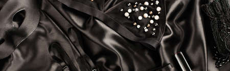 Top view of bra near sexual mask and lipstick on black satin background, bannerの写真素材