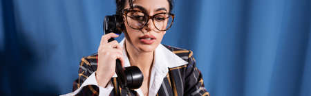 stylish newswoman in vintage clothes and eyeglasses holding handset on blue background, bannerの写真素材