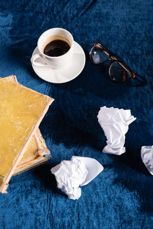 top view of tattered books, crumpled paper, eyeglasses and coffee cup on blue velour tableclothの写真素材