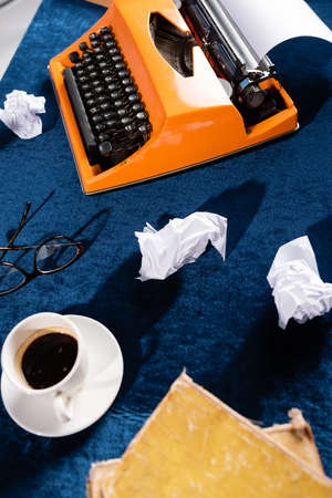top view of coffee cup near vintage typewriter, eyeglasses and crumpled paper on blue velour tableclothの写真素材