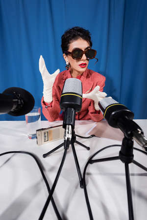 microphones near vintage style woman in sunglasses gesturing during interview on blue backgroundの写真素材