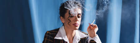 brunette woman in vintage clothes smoking on blue background, bannerの写真素材
