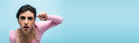 curious woman with open mouth pointing with finger at camera isolated on blue, bannerの写真素材