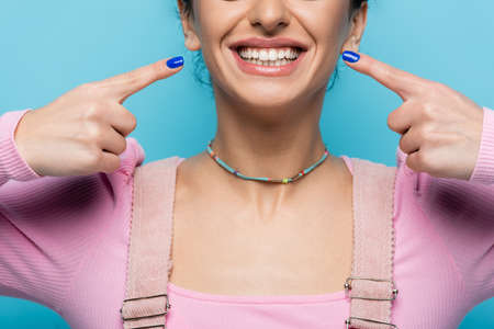 cropped view of happy woman pointing at own smile isolated on blueの写真素材