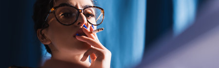 stylish woman in vintage eyeglasses smoking on blue background, bannerの写真素材