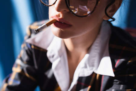 partial view of blurred vintage style woman smoking on blue backgroundの写真素材