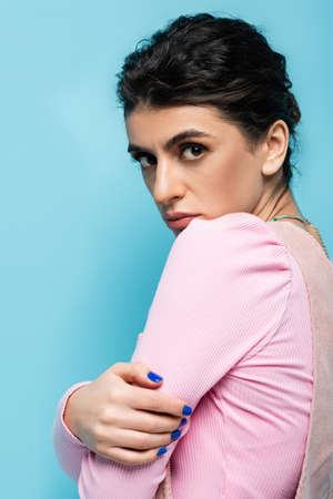 offended brunette woman looking at camera isolated on blue