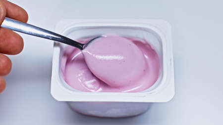 cropped view of man holding spoon near container with yogurt on whiteの写真素材