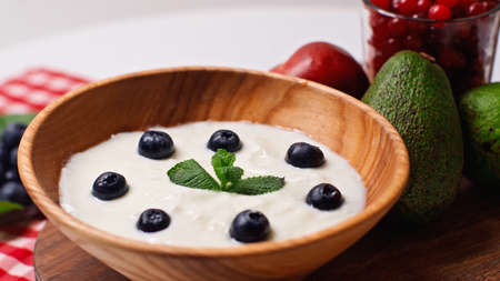 fresh fruits near wooden bowl with yogurt and blueberries on whiteの写真素材