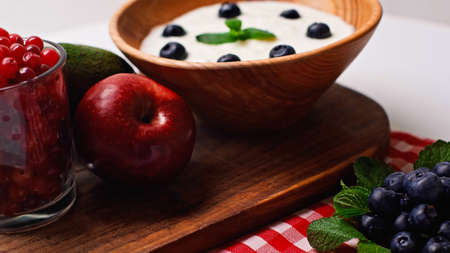 fresh fruits, peppermint and berries near wooden bowl with yogurt on whiteの写真素材