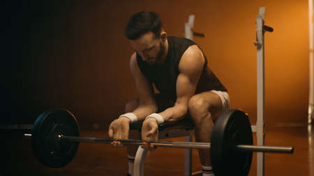 Muscular man training with barbell on flat bench on dark backgroundの写真素材
