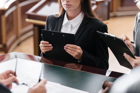 partial view of prosecutor and attorney with clipboards near blurred judge in courtの写真素材