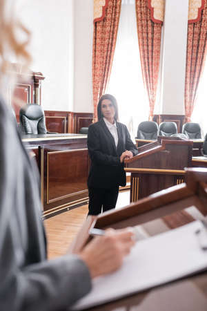 brunette witness looking at blurred attorney writing during litigation