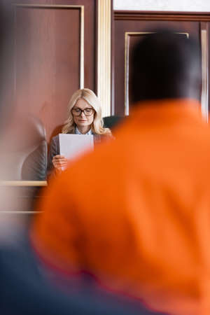 advocate with document near accused african american man in courtroom on blurred foreground
