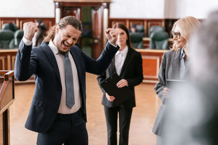 excited businessman shouting and showing win gesture near attorney in courtの写真素材