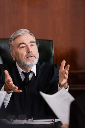 senior judge pointing with hands while talking to blurred prosecutor with lawsuit