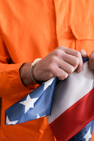 cropped view of man in jail uniform and handcuffs tearing american flag, justice conceptの写真素材