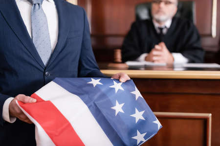 lawyer in suit holding usa flag in courtroom near senior judge on blurred backgroundの写真素材