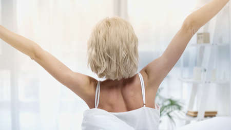 back view of blonde woman stretching in bedroomの写真素材