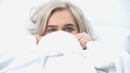 scared woman covering with blanket and watching scary movie in bedの写真素材