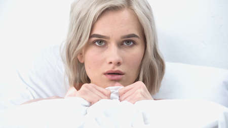 young afraid woman covering with blanket in bedの写真素材