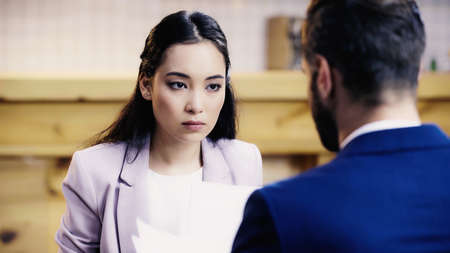 asian businesswoman looking at bearded businessman with documents in cafe