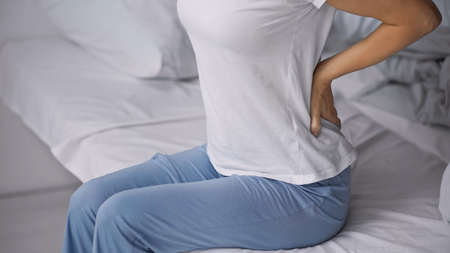 cropped view of woman in pajamas sitting on bed and suffering from hurt in backの写真素材