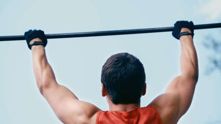 back view of young sportsman doing pull ups on horizontal bar outsideの写真素材
