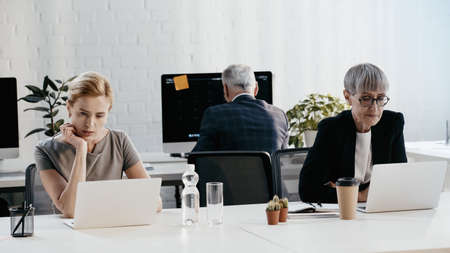 Businesswomen in formal wear using laptops near colleague in officeの写真素材