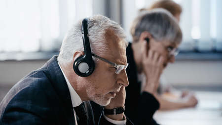 Side view of middle aged businessman in headset working in officeの写真素材