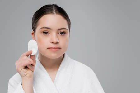 Woman with down syndrome in bathrobe holding cotton pad isolated on greyの写真素材